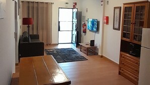 A spacious living area with a wooden bench, a television, and a kitchen area with cabinets. - 2 Bedroom Apartment a Walk from the Beach of Praia da Areia Branca. (Lourinhã)