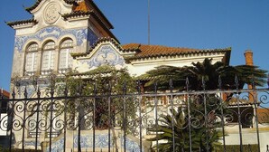A building with ornate blue and white tile work, a tiled roof, and a wrought iron fence in the foreground. - 2 Bedroom Apartment a Walk from the Beach of Praia da Areia Branca. (Lourinhã)