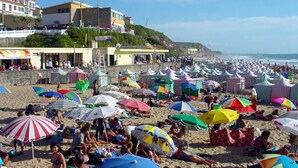 A crowded beach with numerous colorful umbrellas and people relaxing. - 2 Bedroom Apartment a Walk from the Beach of Praia da Areia Branca. (Lourinhã)