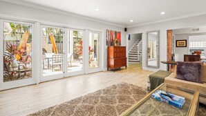 Een ruime woonkamer met een grote schuifpui naar een buitenruimte, een houten kast, een bank met een plaid en een salontafel met een boek.