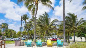 Een strandgebied met kleurrijke Adirondack-stoelen, palmbomen en een parkeerplaats met auto's.