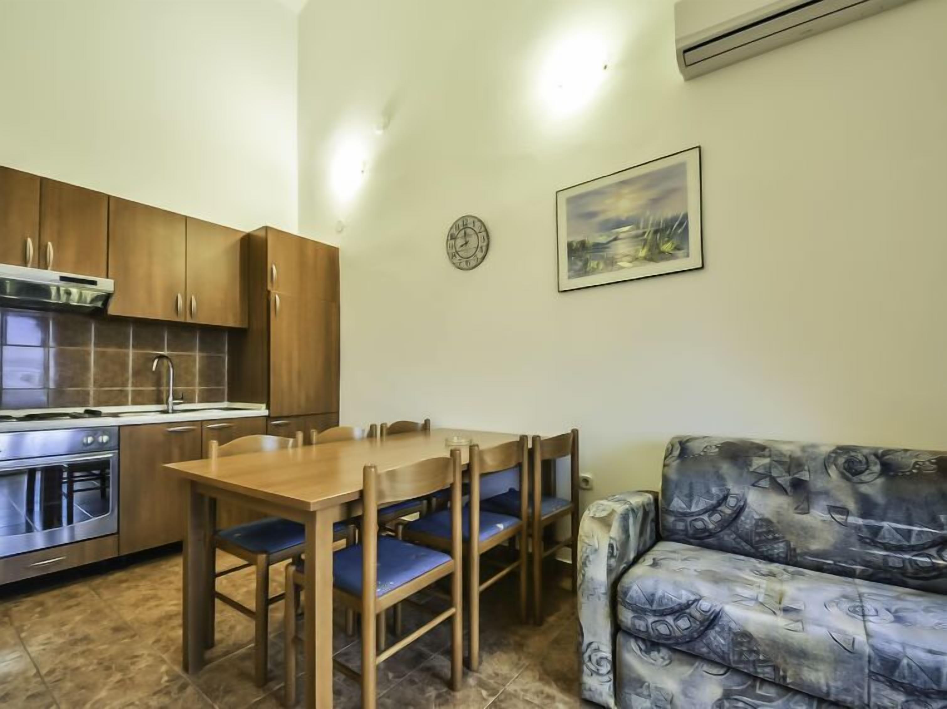 A compact kitchen with wooden cabinets, a stainless steel stove, and a dining table with blue chairs.