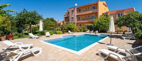A swimming pool with lounge chairs, surrounded by a garden and a building with balconies.
