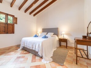 A bedroom with a bed, wooden headboard, two bedside tables with lamps, a wooden dresser, and a window with wooden shutters. - Can Monjo by Interhome (Andratx)