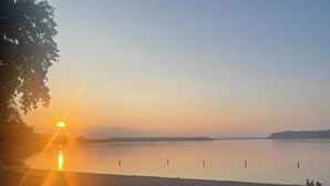 Ein ruhiger Strand bei Sonnenuntergang, mit klarem Himmel, ruhigem Wasser und Felsen im Vordergrund.