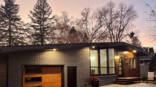 Ein modernes Haus mit Ziegelaußenwand, großen Fenstern und einer Holztür zur Garage.