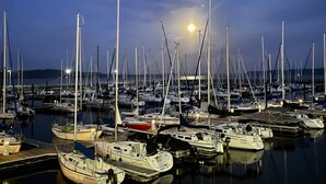 Eine Marina mit mehreren Schiffen an den Liegeplätzen, bewölkter Himmel und ein sichtbarer Mond.