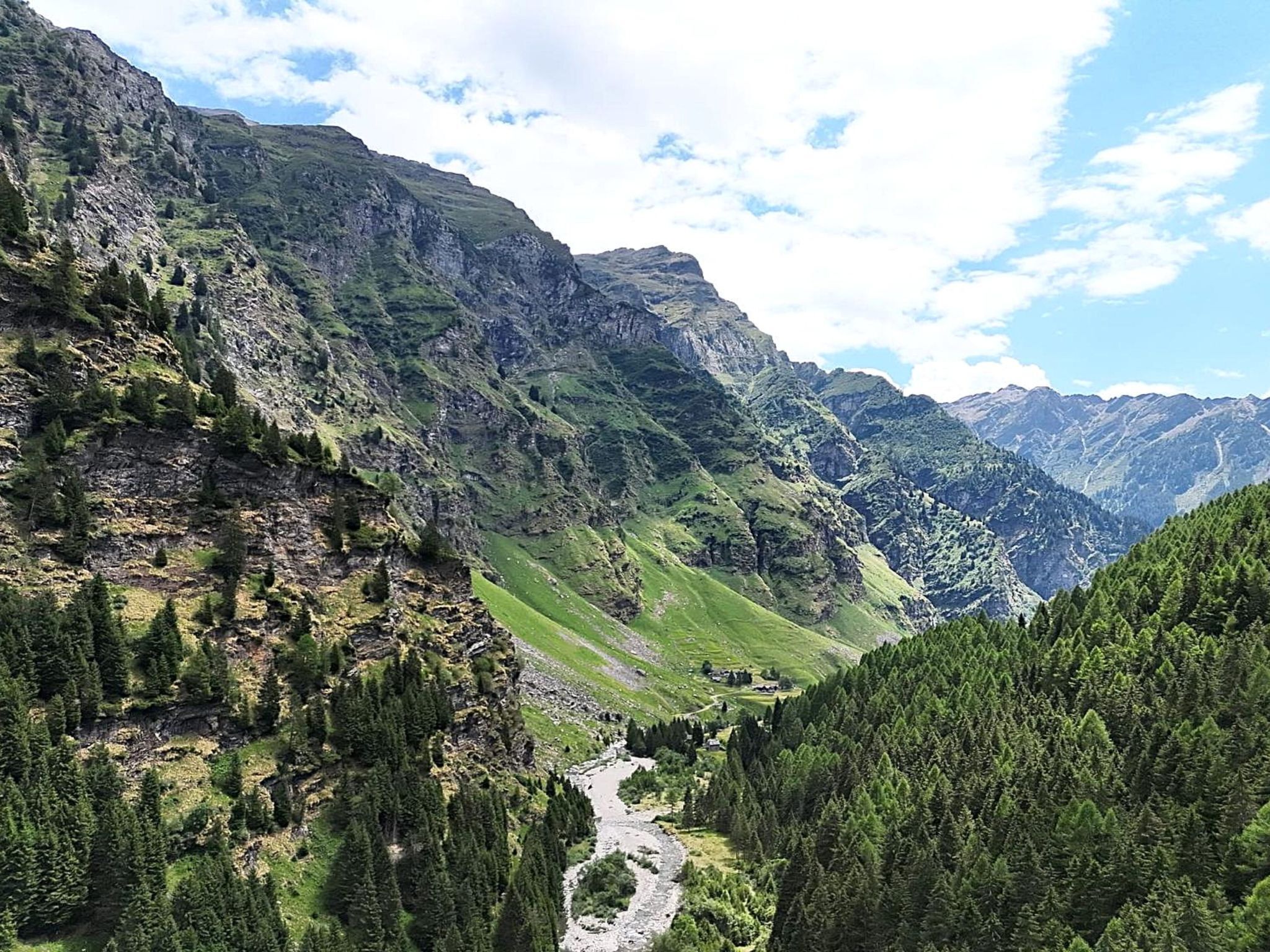 Un paysage montagneux, traversé par une rivière qui serpente à travers une vallée, le tout entouré de forêts denses et de falaises abruptes.