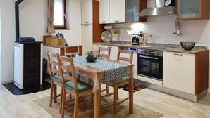 A modern kitchen with white cabinets, a stainless steel range hood, and a built-in oven. There is a dining table with chairs and a small plant on it. - Open Space with Patio "Lety" by Interhome (Malvaglia)