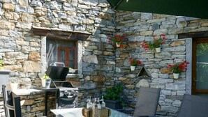An outdoor patio with a stone wall, a grill, a table set for dining, and potted plants. - Open Space with Patio "Lety" by Interhome (Malvaglia)