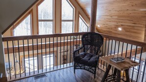 Un balcone in legno con una sedia in vimini nero e un tavolino con un libro.