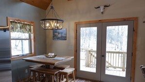 Un tavolo da pranzo in legno con panche, un lampadario e una porta che dà su un patio.