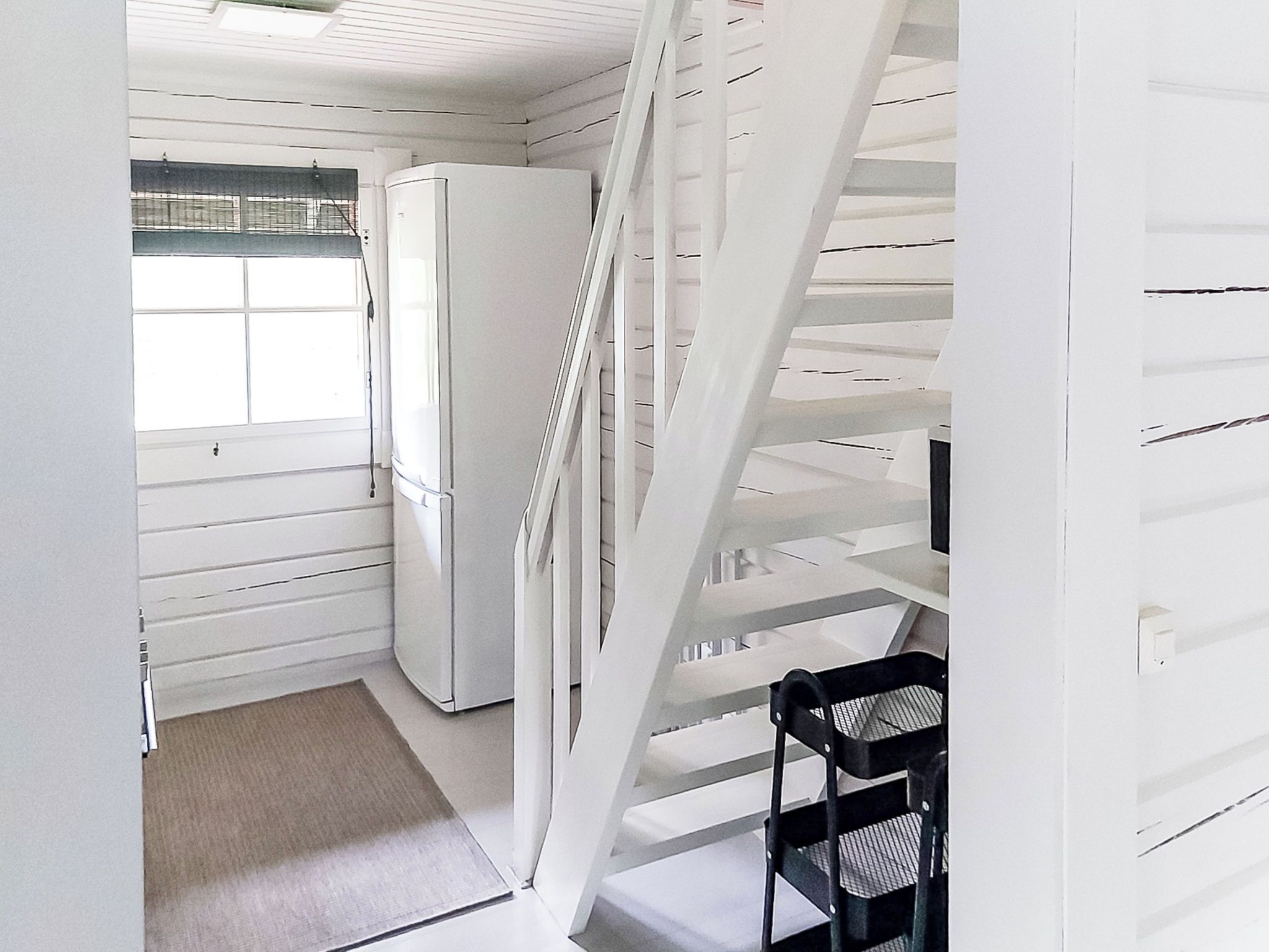 Ein schmales Entree mit einer weißen Treppe, einem Kühlschrank und einem Sessel.
