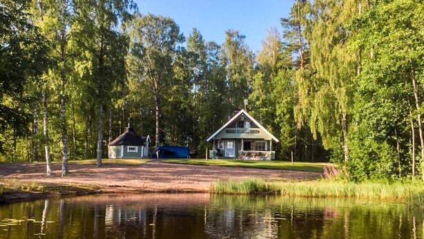 A lakeside cabin with a dock, surrounded by dense trees and a calm water body.