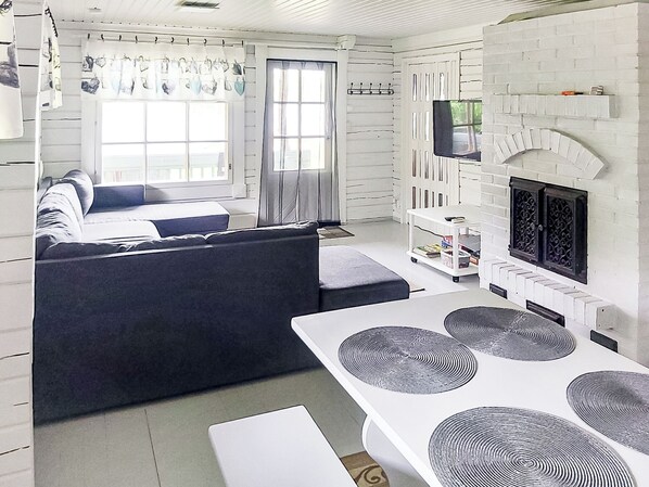 A modern living room with a sofa, a dining table with placemats, a fireplace, and a television. - Villa koivumäki by Interhome (Kankaanpää)