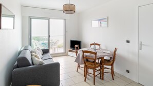 A modern living room with a grey sofa, a dining table set for four, and a TV. - Apartment Claire by Interhome (Arcachon)