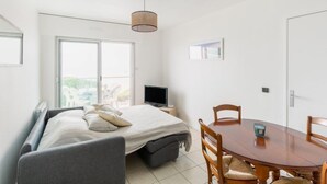 A bedroom with a bed, a TV, a dining table with chairs, and a large window. - Apartment Claire by Interhome (Arcachon)