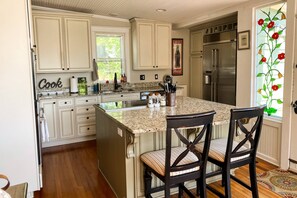 A kitchen with white cabinets, a granite countertop, stainless steel appliances, and two upholstered chairs.
