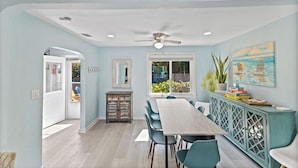 A dining area with a long table, teal chairs, a cabinet with open doors, and a ceiling fan. - 2-Min Walk to Beach, 3 Cars, 3BR Family Escape walkable to Boardwalk (Daytona Beach)