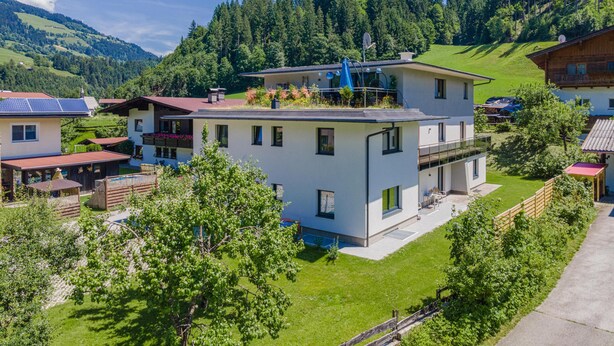 Ein modernes, zweistöckiges Haus mit Flachdach, umgeben von üppiger Vegetation und einer Bergkulisse.