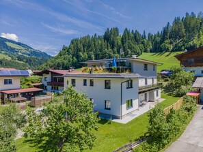 A modern two-story house with a flat roof, surrounded by lush greenery and a mountainous backdrop. - Beautiful apartment 5 min from the centre (Hopfgarten im Brixental)