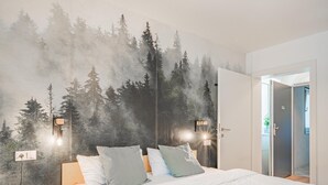 Ein Schlafzimmer mit einem Bett, Kissen, einem Nachttisch, einem Wandgemälde von einem Wald und zwei Wandleuchten.