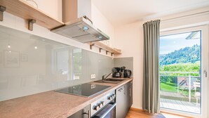 Una cuina moderna amb una illa gran, forn integrat i vista a un paisatge verd a través d'una porta corredissa de vidre.