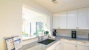 Una cocina con armarios blancos, encimera de granito, fregadero y cafetera.