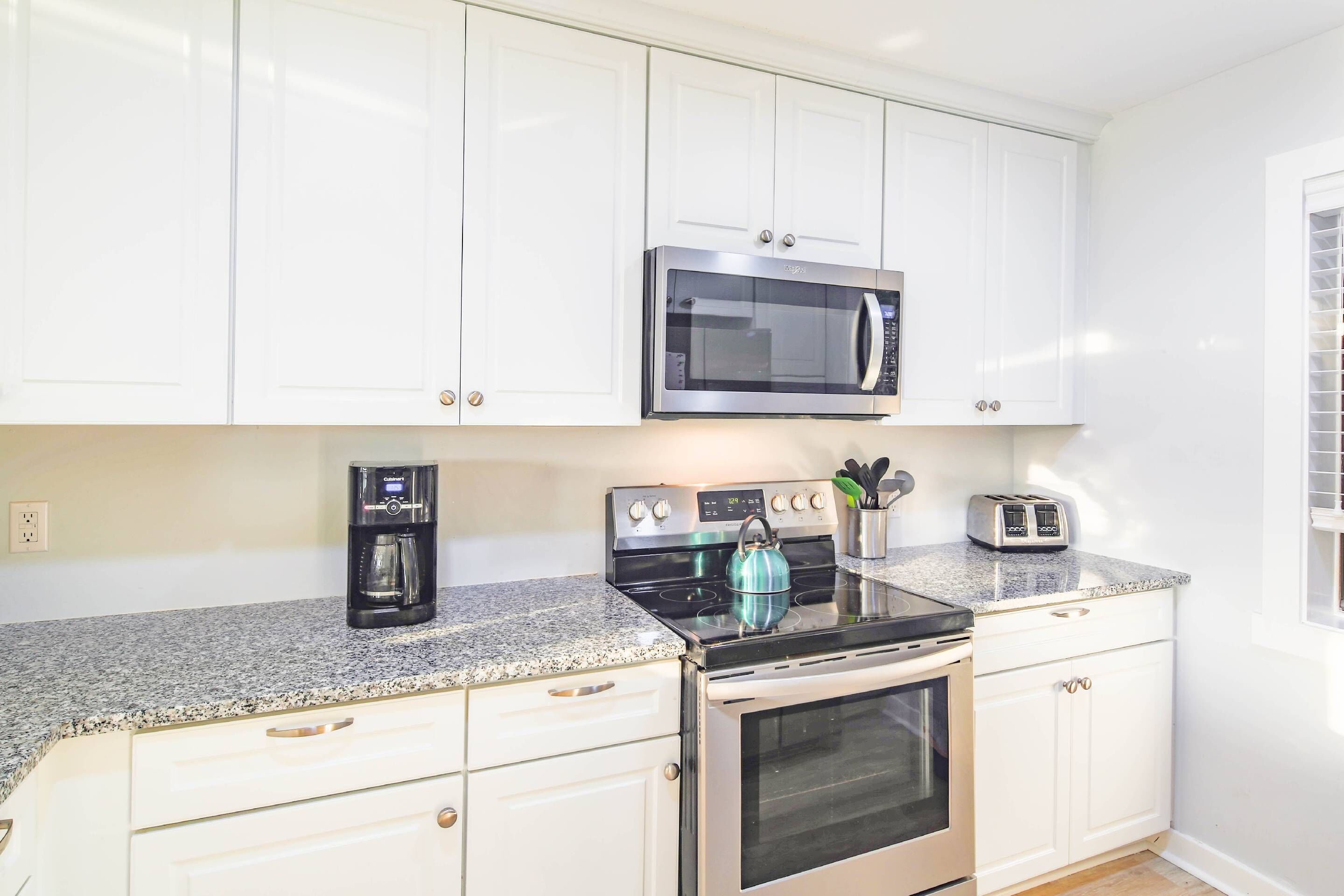 A kitchen with white cabinets, a stainless steel microwave, a coffee maker, a kettle, and a toaster.