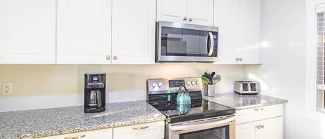 A kitchen with white cabinets, a stainless steel microwave, a coffee maker, a kettle, and a toaster.