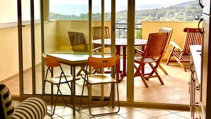A balcony with a table and chairs, a view of the landscape, and a door with a handle.