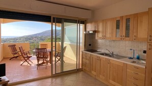 A balcony with a table and chairs, a kitchen with wooden cabinets, and a view of the landscape.