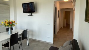 Een moderne woonkamer met een eethoek, een flatscreen televisie aan de muur en een gang die naar andere kamers leidt.