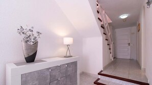 A modern hallway with a white console table, a vase with dried flowers, and a floor lamp. - Parque Santiago II 131 - One Bed Duplex with Pool (Playa de las Americas)