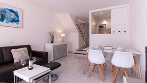 A modern living room with a sofa, a coffee table, and a dining area with white chairs and a table. - Parque Santiago II 131 - One Bed Duplex with Pool (Playa de las Americas)