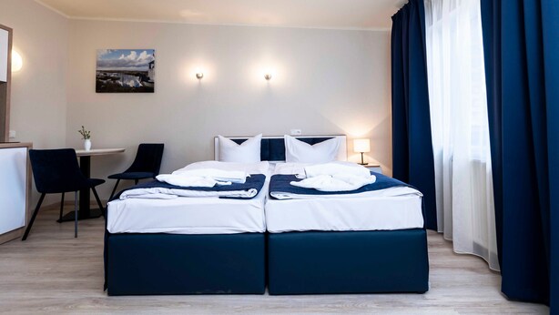Habitació d'hotel amb un llit doble, una escriptori amb una cadira, una taula petita i un quadre a la paret.