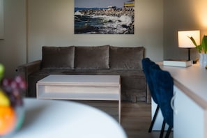 Una sala de estar con un sofá, una mesa de centro, una lámpara y un cuadro de una escena costera.