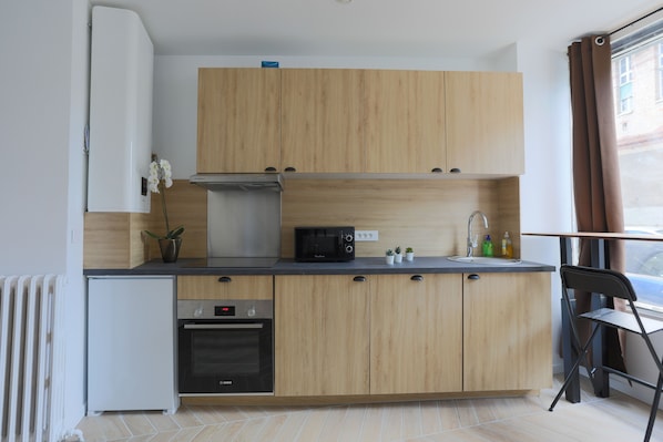 A compact kitchen with wooden cabinets, a built-in microwave, a sink, and a compact refrigerator.
