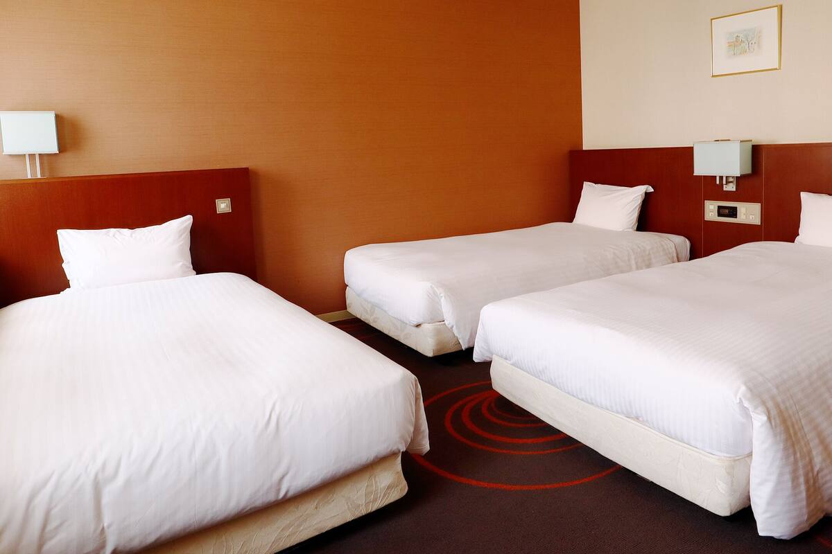 A hotel room with three single beds, a wooden headboard, a red carpet, and a wall-mounted lamp.