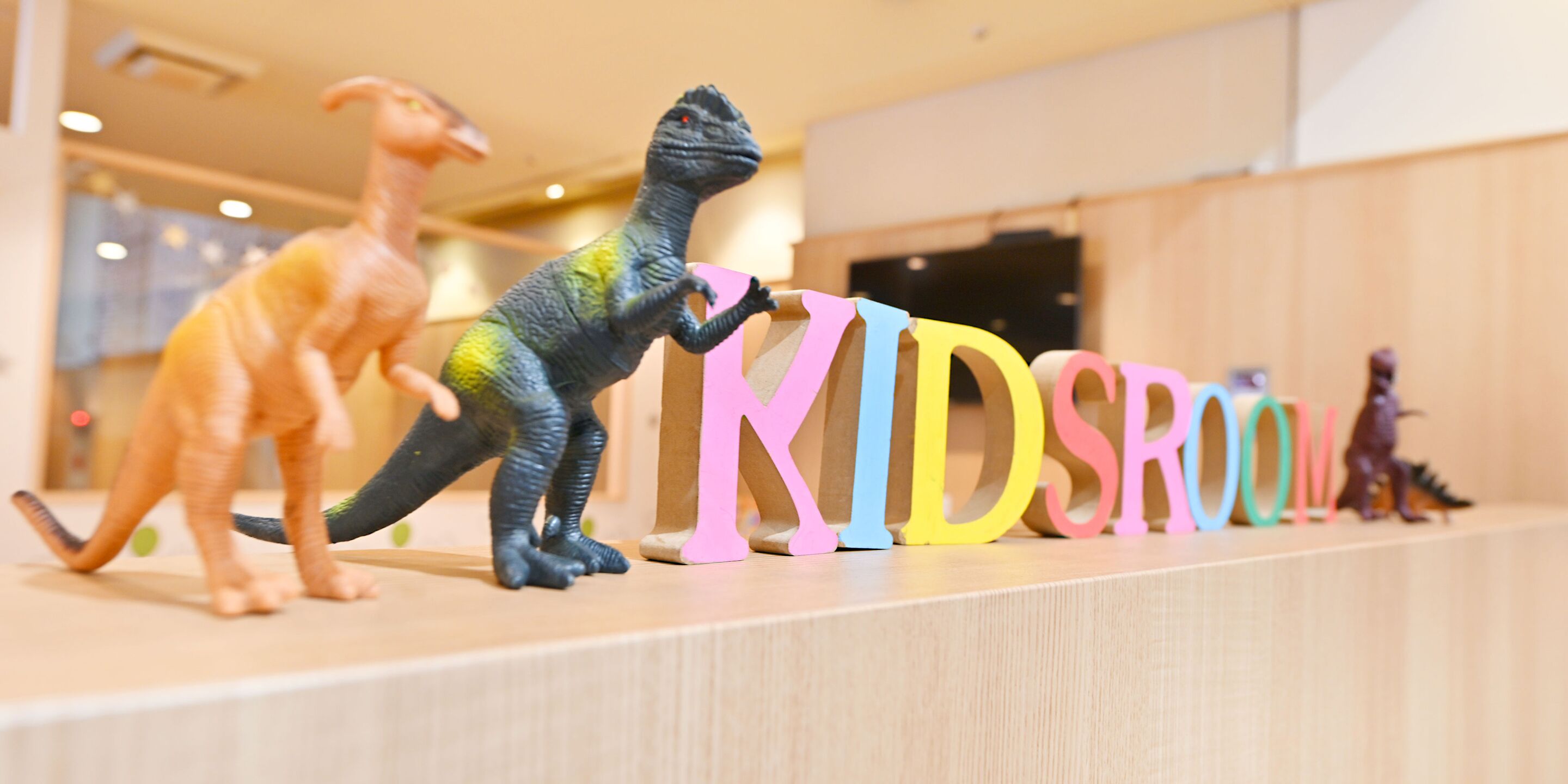 A display of dinosaur toys and colorful letters spelling "KIDSROOM" on a shelf.