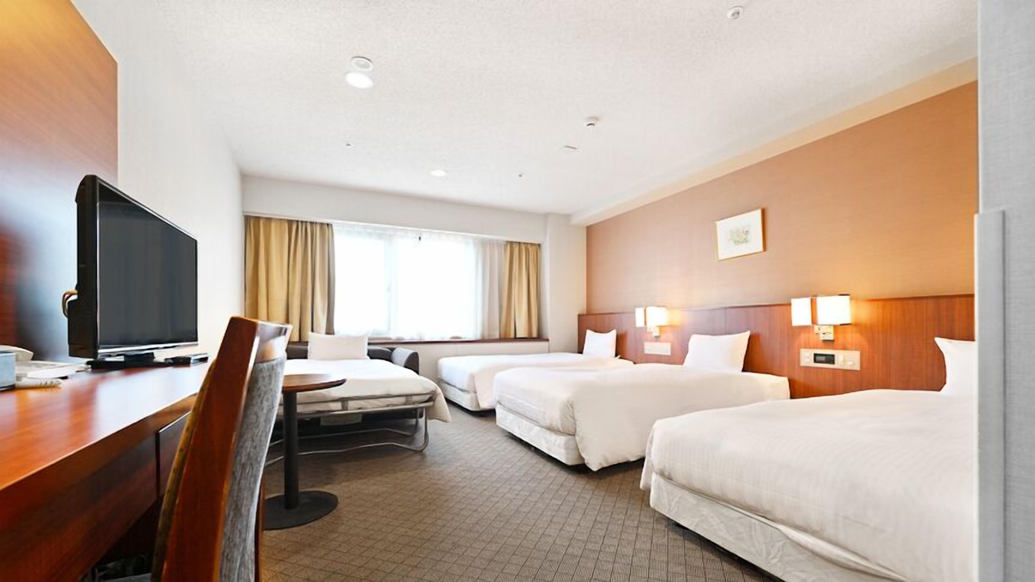 A hotel room with a desk, TV, two beds, and a window with curtains.