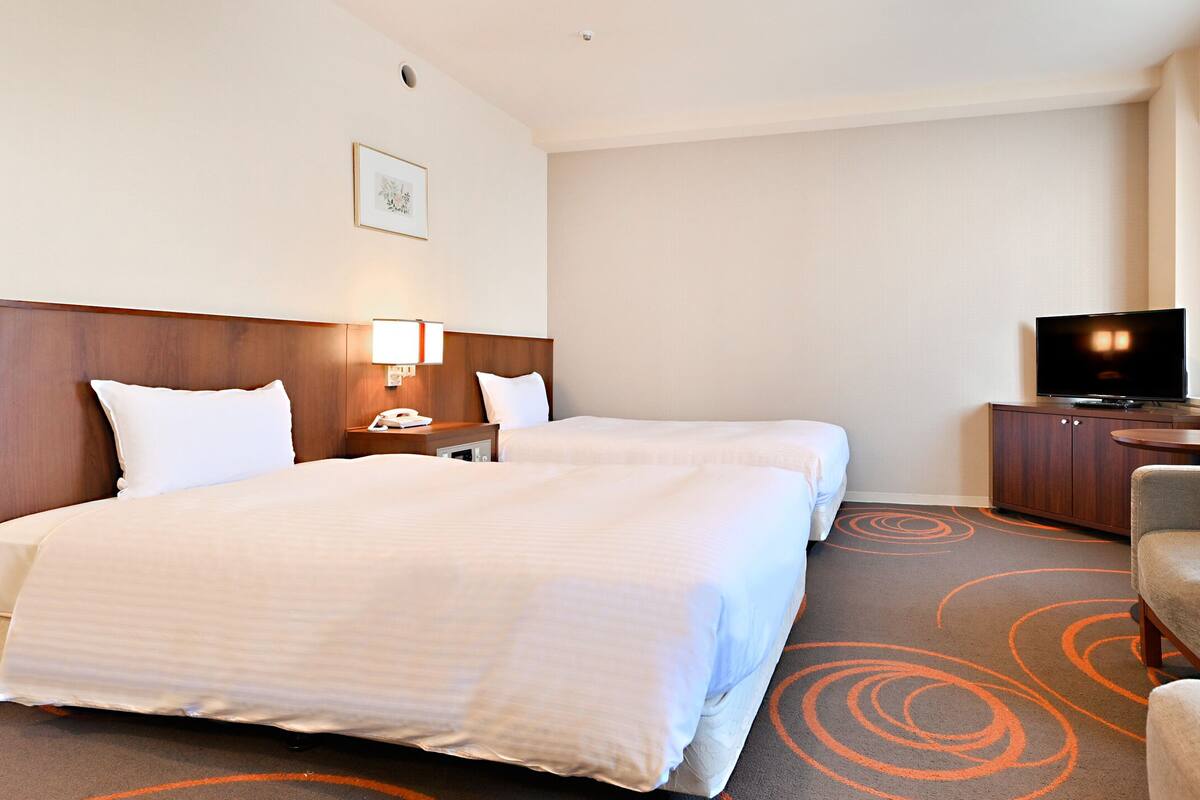 A hotel room with two beds, a TV, a desk, and a chair.