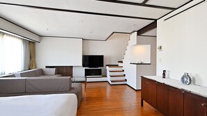 A modern living room with a sofa, TV, wooden flooring, and a staircase.