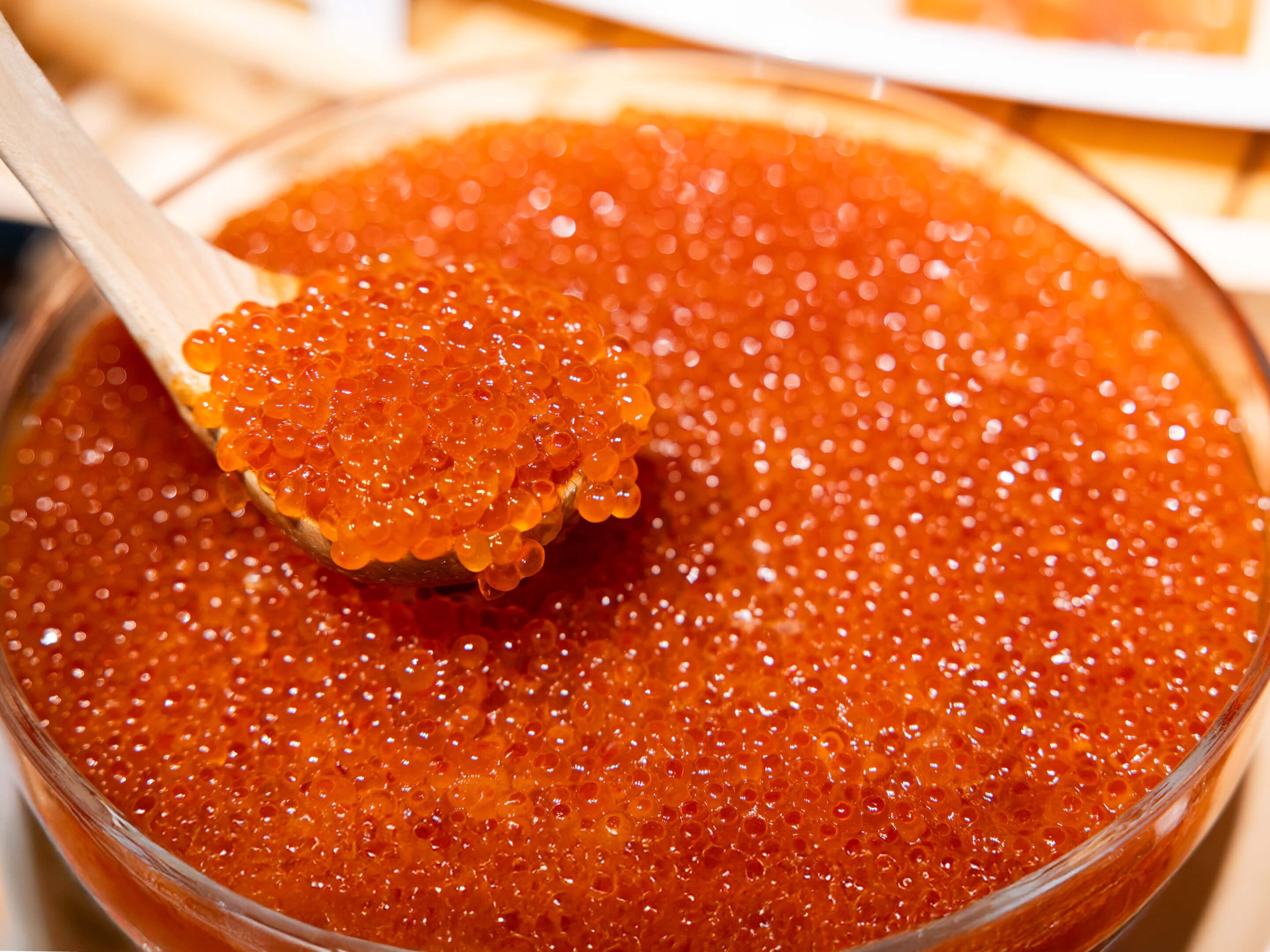 A bowl of red caviar with a wooden spoon.