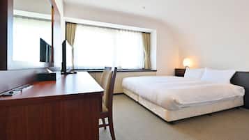 Et hotelværelse med seng, skrivebord, stol, fjernsyn og et vindue med gardiner.
