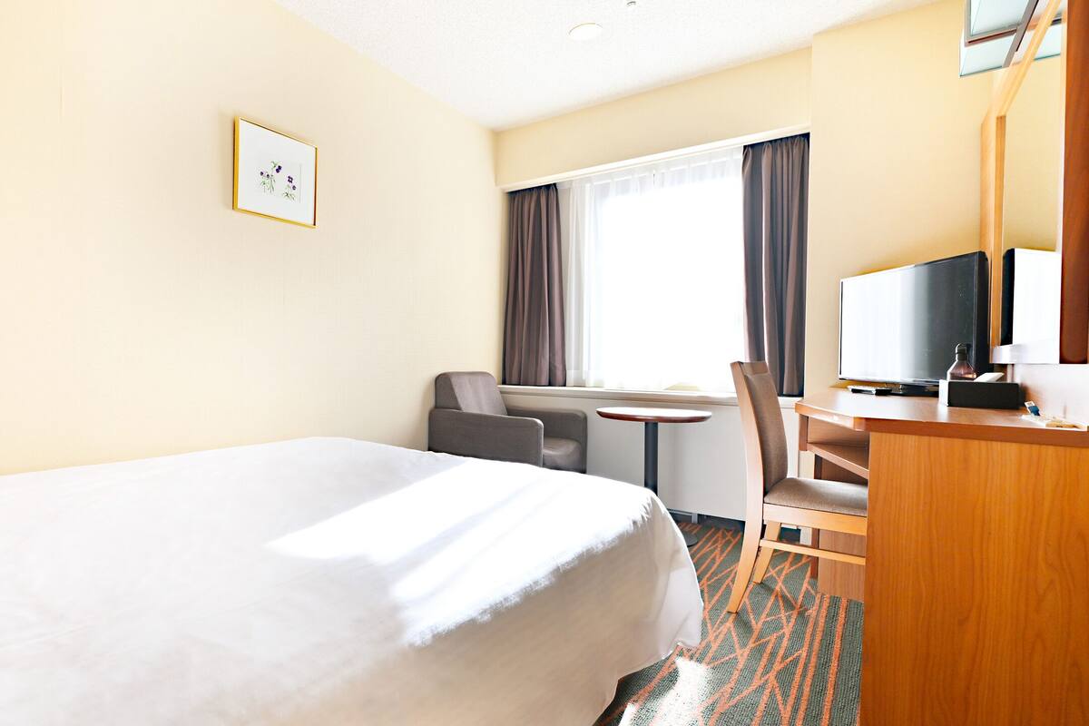 A hotel room with a large bed, a desk with a chair, a television, and a window with curtains.