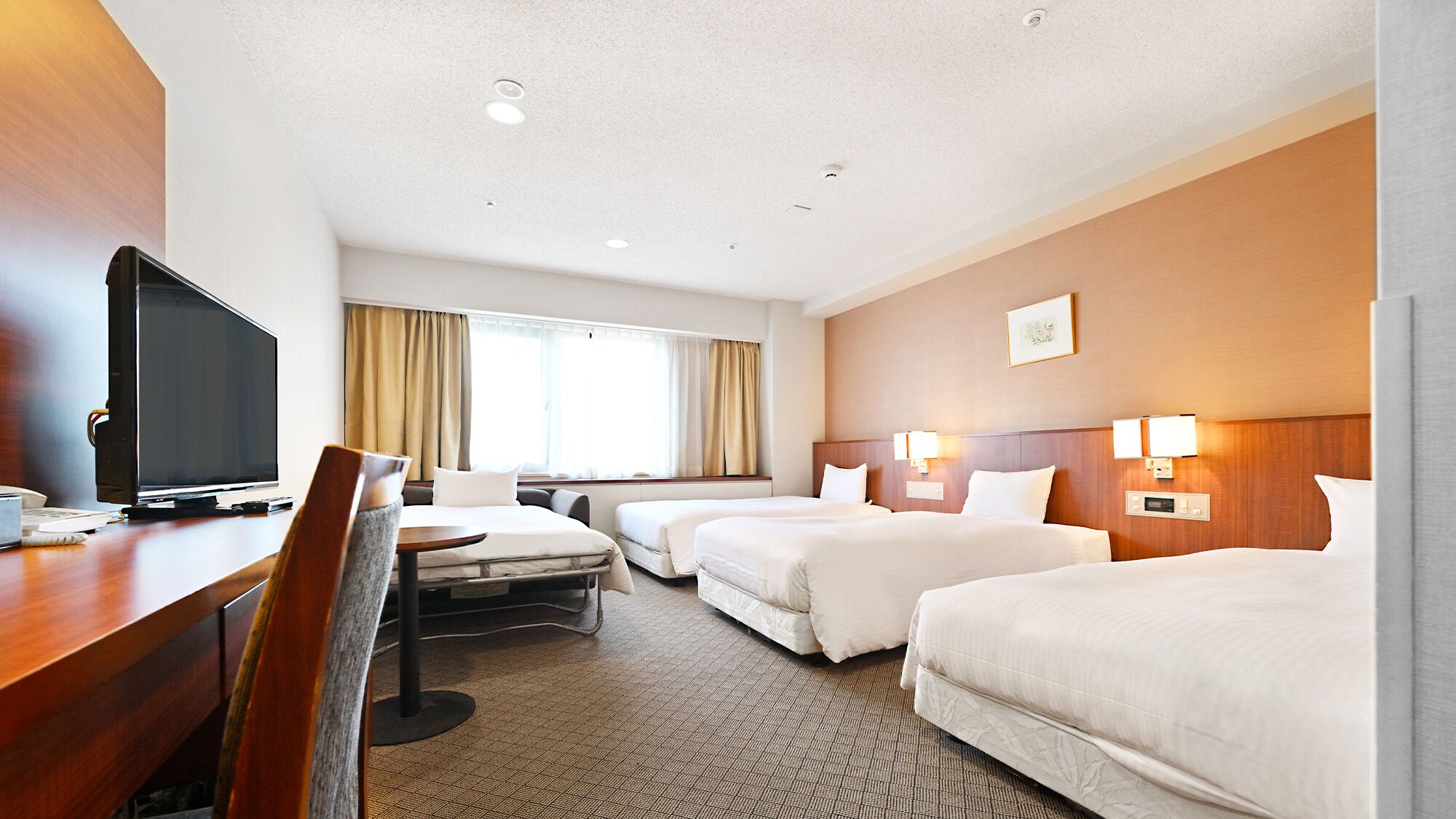 A hotel room with a desk, television, two beds, a chair, and a window with curtains.