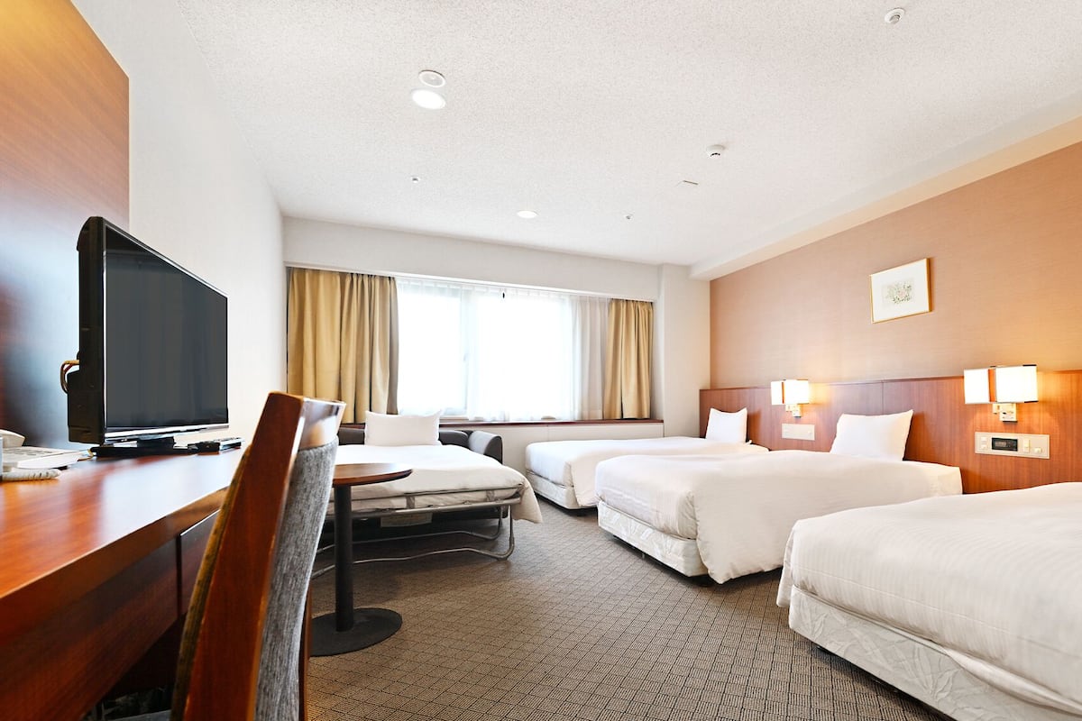 A hotel room with a desk, television, two beds, a chair, and a window with curtains.