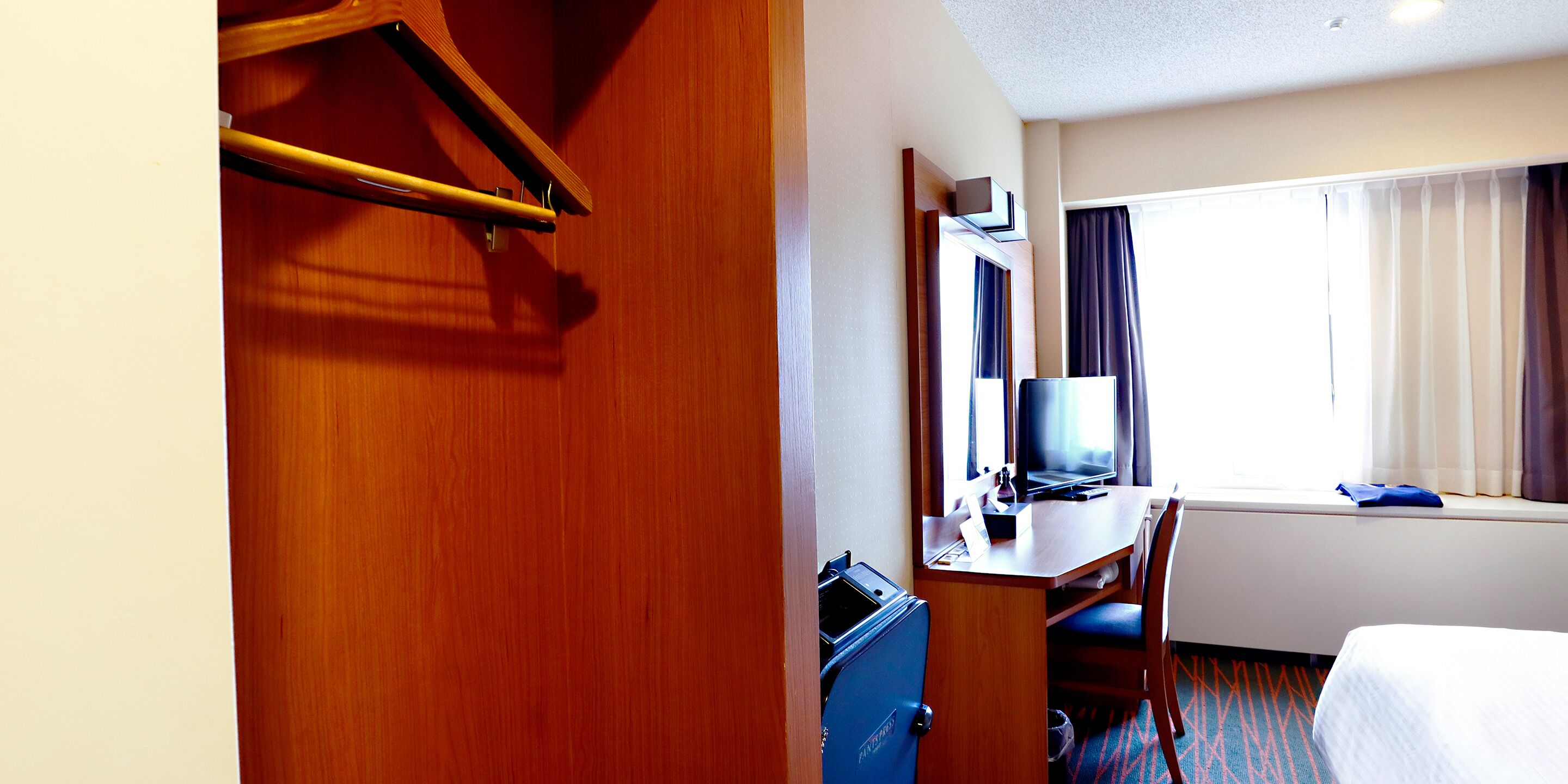A hotel room with a wooden desk, a television, a bed, and a window with curtains.