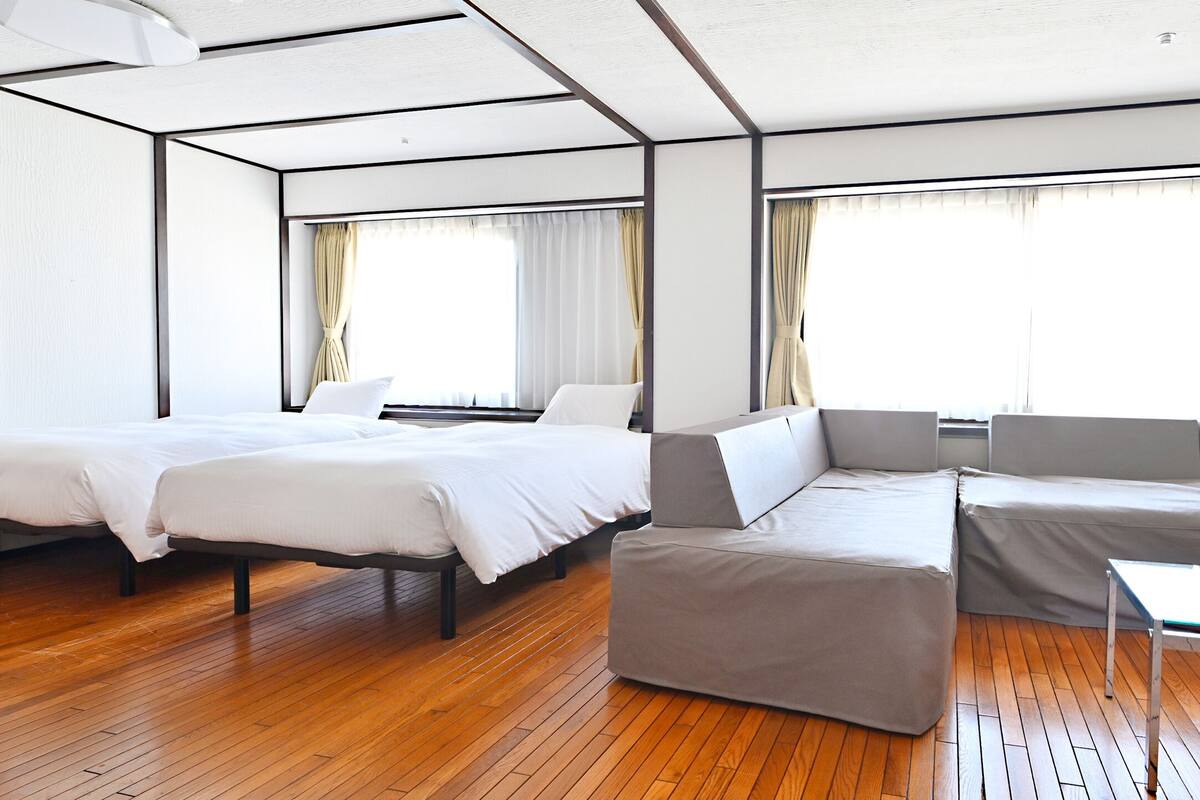 A modern hotel room with a large bed, a sofa, and a glass coffee table.